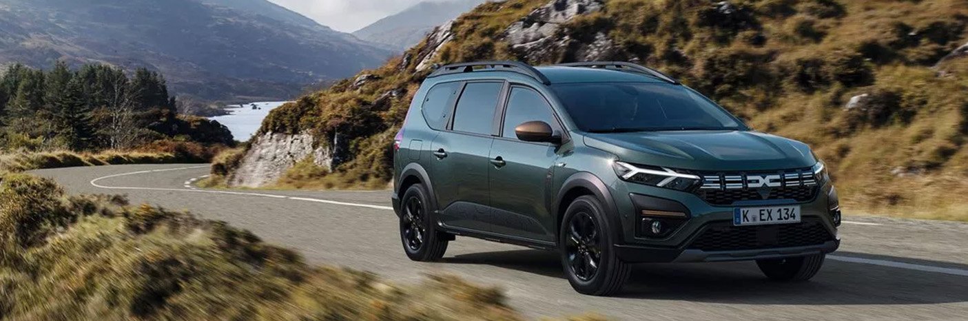 Ein mittelgroßes SUV in grün fährt auf einer kurvenreichen Straße in einer Berglandschaft.