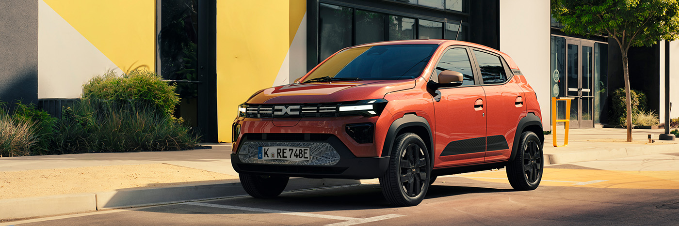 Ein roter SUV parkt vor einem modernen Gebäude mit buntem Design, umgeben von Pflanzen.