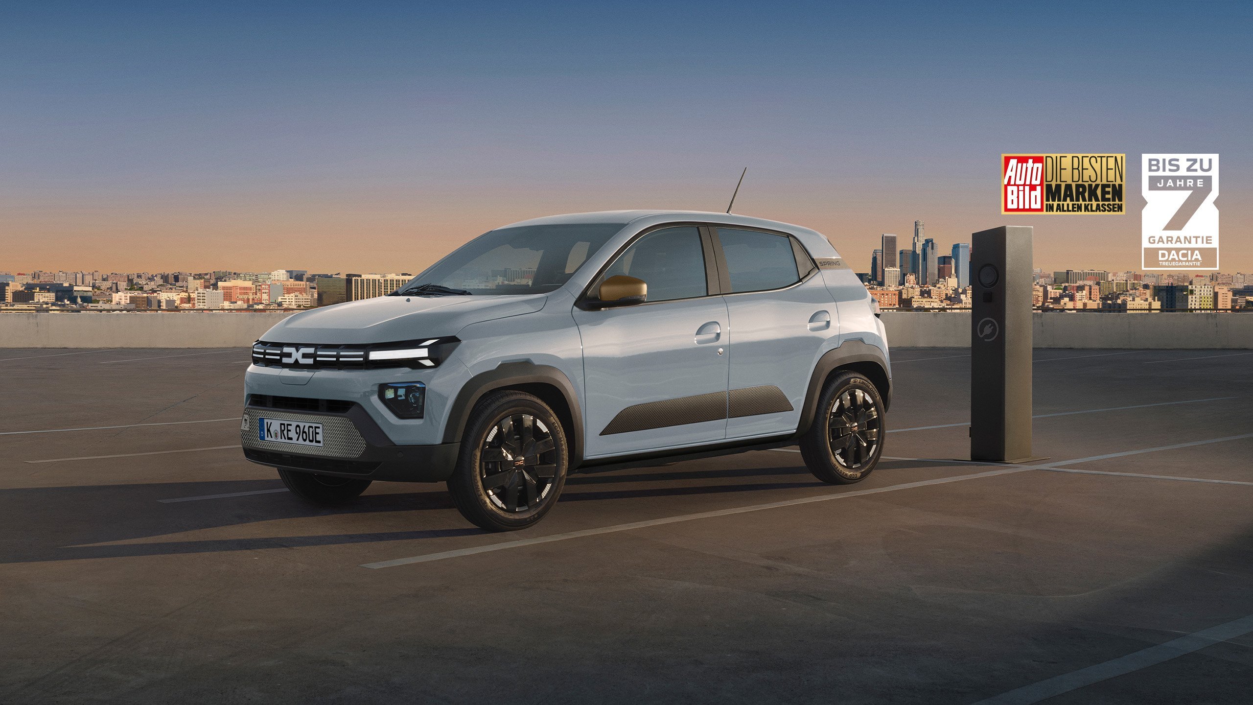 Ein moderner Elektro-SUV auf einem Parkplatz mit Stadtlandschaft im Hintergrund. Besondere Merkmale und Auszeichnungen sind sichtbar.
