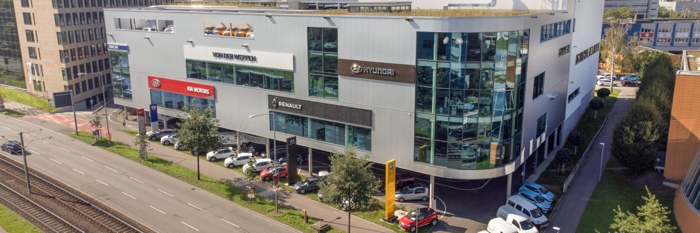 Moderne Automobilhaus-Fassade mit Markenlogos und Autos auf dem Parkplatz.