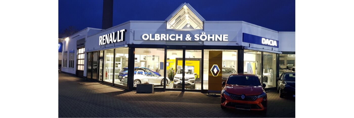 Renault Autohaus Olbrich & Söhne bei Nacht, mit beleuchtetem Schild und Autos im Fenster.