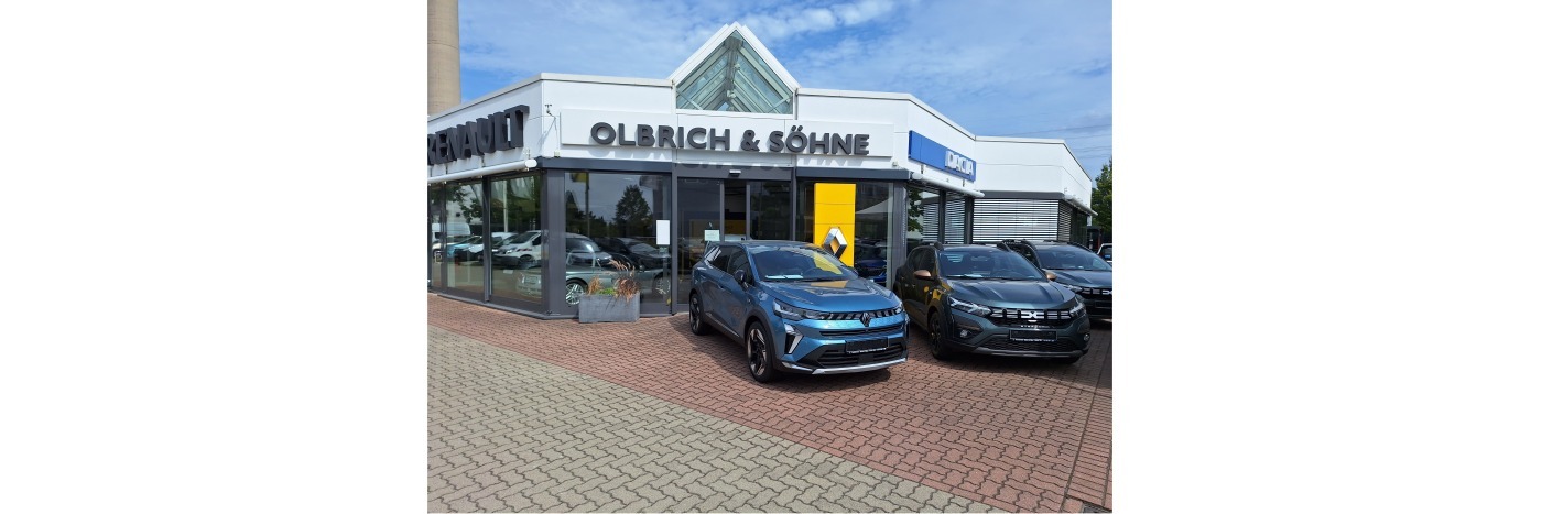 Autohaus Olbrich & Söhne mit mehreren Fahrzeugen auf der Ausstellung. Helle Fassade und wolkiger Himmel.