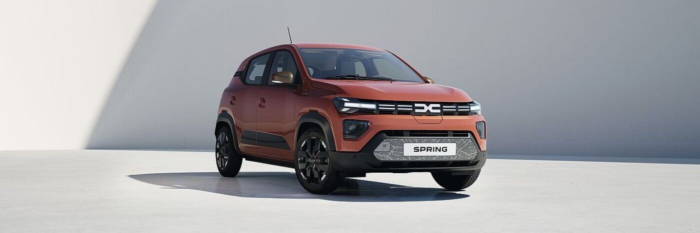 Ein elektrisches Auto der Marke Dacia, Modell Spring, in Rot, steht vor einer hellen Wand.