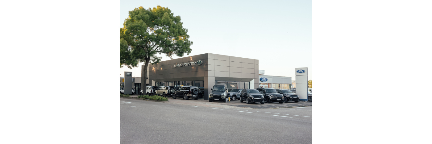 Autohaus mit mehreren Fahrzeugen und Bäumen vor dem Gebäude, ideal für den Autokauf oder Service.