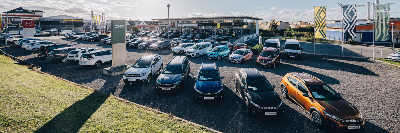 Autos auf einem Autohof, verschiedene Modelle und Marken, Verkaufsfläche mit Werbebannern.