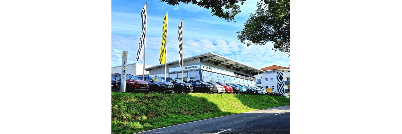 Autohaus mit mehreren Fahrzeugen vor einem modernen Gebäude, blauer Himmel und Fahnen sichtbar.