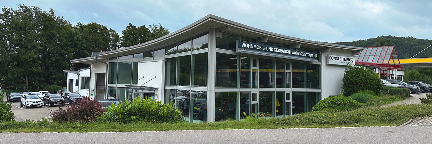 Ansicht eines Wohnmobil- und Gebrauchtwagenzentrums mit mehreren Autos und umgebenden Bäumen.