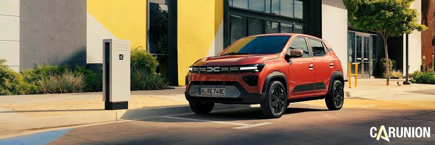 Ein rotes Elektroauto parkt vor einem modernen Gebäude mit einer Ladestation in der Nähe.