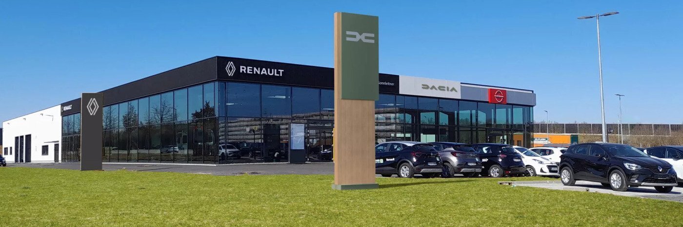 Renault und Dacia Autohaus mit modernen Fahrzeugen, großen Fenstern und grüner Wiese im Vordergrund.