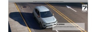 Ein silberner Dacia Spring fährt auf einer Straße, Werbebanner im Vordergrund.