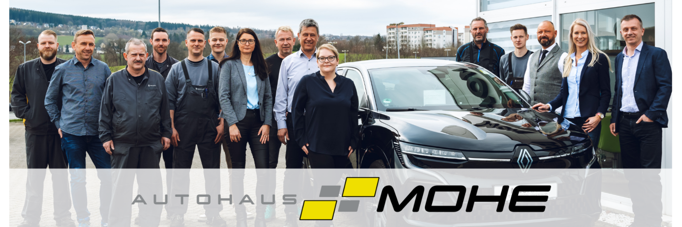 Gruppe von Mitarbeitern vor einem schwarzen Renault im Autohaus Mohe, umgeben von einer Landschaft mit Gebäuden.