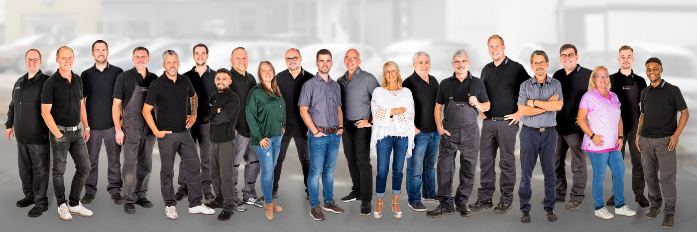 Gruppenfoto von 20 Mitarbeitern in einheitlichen Outfits, lächelnd, vor einem unscharfen Hintergrund.