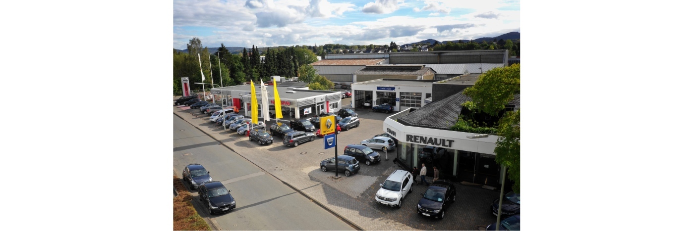 Luftaufnahme eines Autohauses mit Renault-Logo, vielen Fahrzeugen und bunten Werbefahnen.