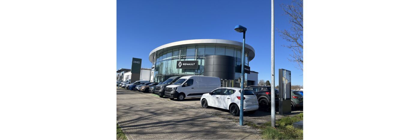 Renault Autohaus mit mehreren Fahrzeugen auf dem Parkplatz bei klarem blauen Himmel.