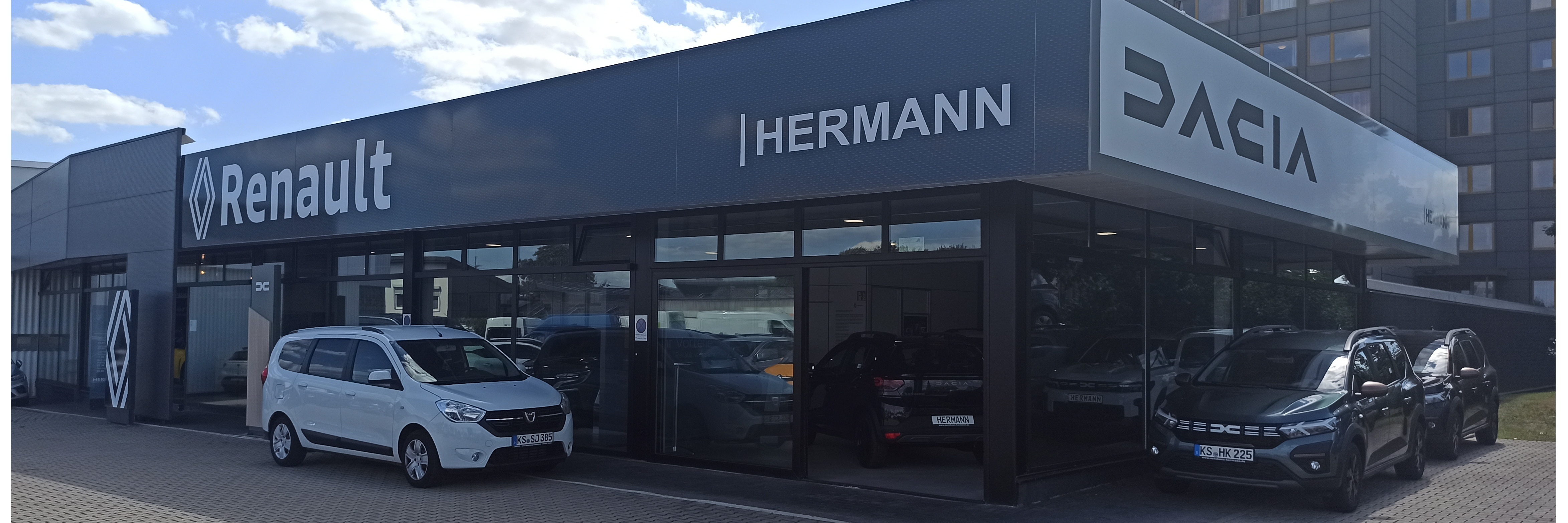Renault und Dacia Autohaus Hermann mit verschiedenen Autos vor dem Gebäude an einem sonnigen Tag.